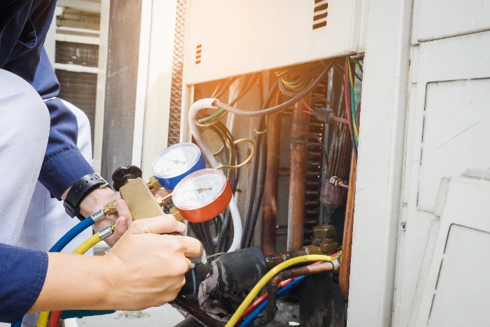 A person uses HVAC manifold gauges to check and service the cooling system of an air conditioning unit.