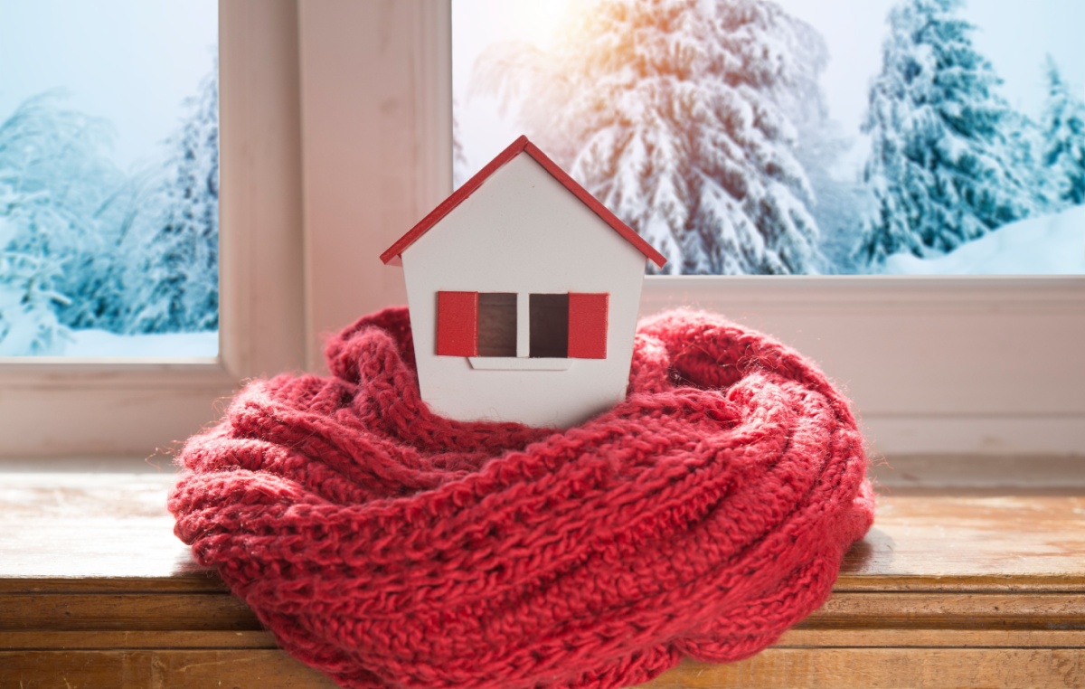 a miniature house wrapped in a scarf on the windowsill with a winter scene behind it