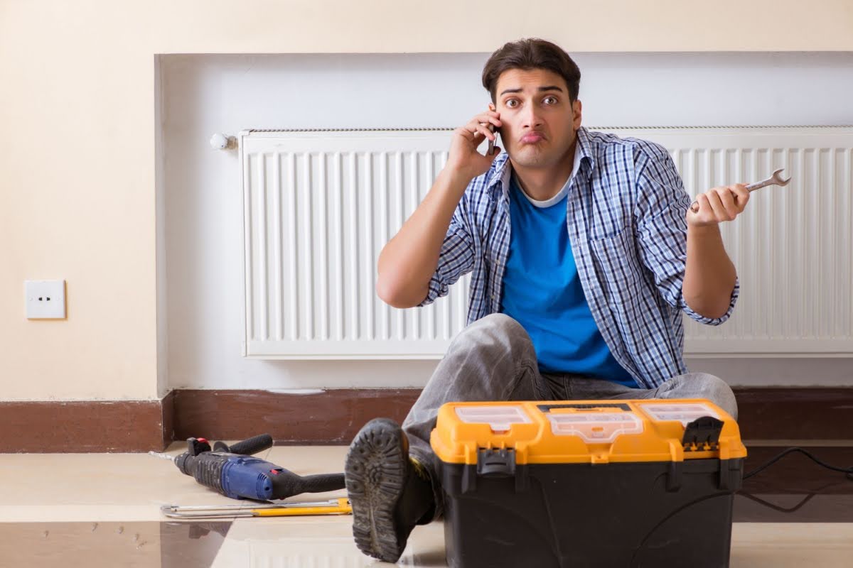 a confused man sitting on the floor by his radiator with a toolbox and tools around him