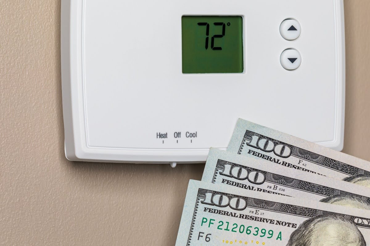 A stack of cash fanned out in front of a thermostat to show how expensive heating repairs can be